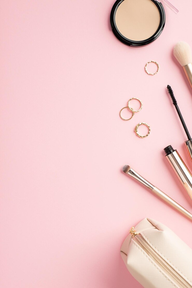 Compõem o conceito de beleza Foto vertical vista superior de anéis de ouro pó compacto pincéis de maquiagem rímel e bolsa cosmética em fundo rosa pastel com espaço vazio