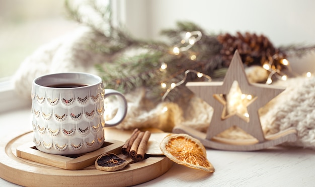 Composição aconchegante com uma xícara de natal com uma bebida quente e canela em um fundo desfocado. conceito de aconchego de inverno em casa.