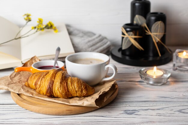 Foto composição aconchegante hygge com croissant caseiro fresco e café na mesa de madeira branca com velas, livros e malhas