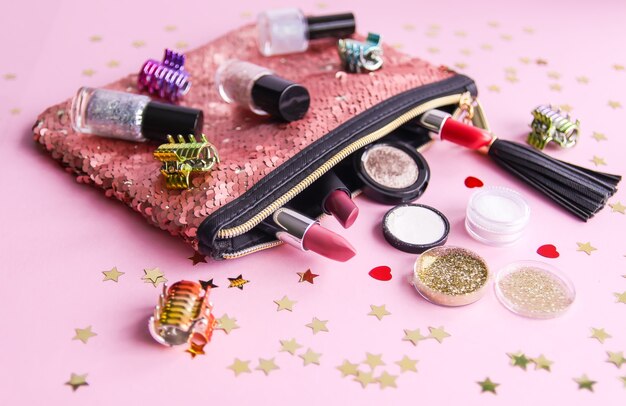 Composição brilhante de acessórios de moda. Bolsa cosmética de lantejoulas glitter com batons, esmaltes e outros objetos. Objeto em fundo pastel suave com enfeites decorativos. Camada plana, vista superior.