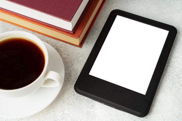 Composição com livro de capa dura de leitor de ebook moderno e xícara de café na mesa