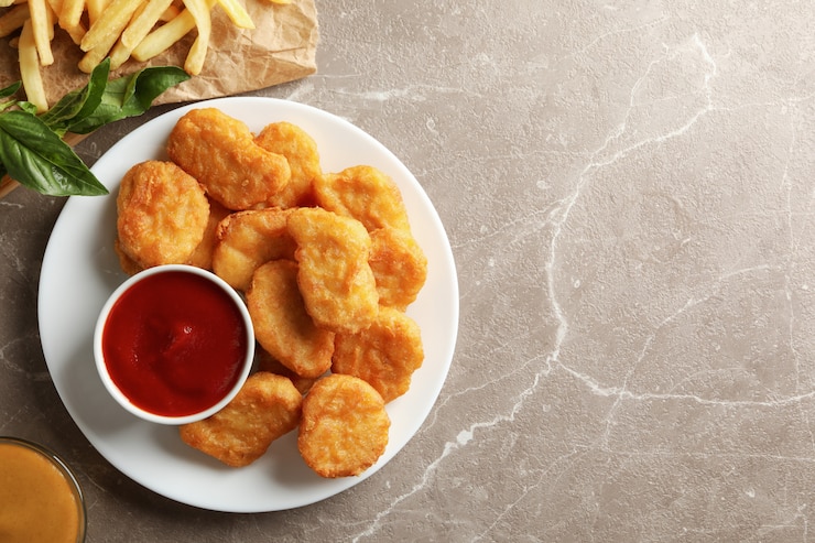 Foto composição com nuggets de frango, batata e molhos na mesa cinza