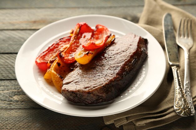 Foto composição com saborosa carne assada e legumes em prato sobre fundo de madeira