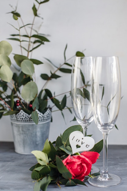 Composição com taça para champanhe. Flores e corações em fundo cinza de concreto.