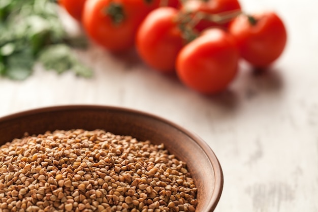 Composição com tigela de cerâmica de trigo sarraceno seco, ovos e tomate.