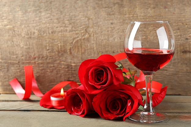 Composição com vinho tinto em copos, rosas vermelhas e coração decorativo em fundo de madeira