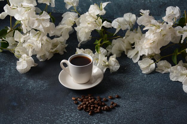 Composição com xícara de café branca, feijão e flores como pano de fundo