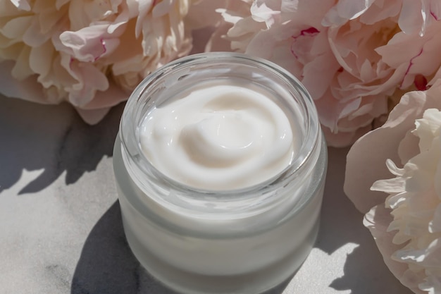 Composição cosmética de flores com frasco de creme facial natural e peônias rosadas em flor em fundo de mármore branco conceito de produtos de beleza orgânicos à base de plantas Close Up