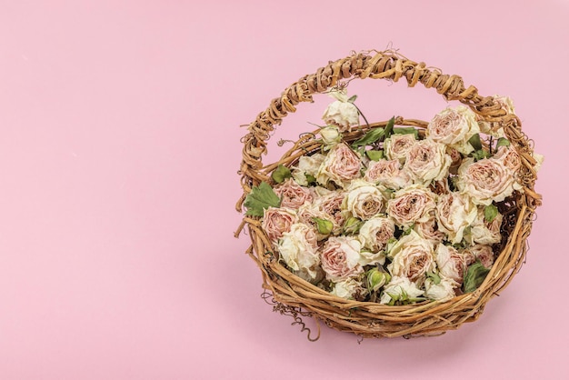 Composição criativa com rosas secas e delicadas em cesta de vime caseira Cartão de saudação de fundo rosa pastel