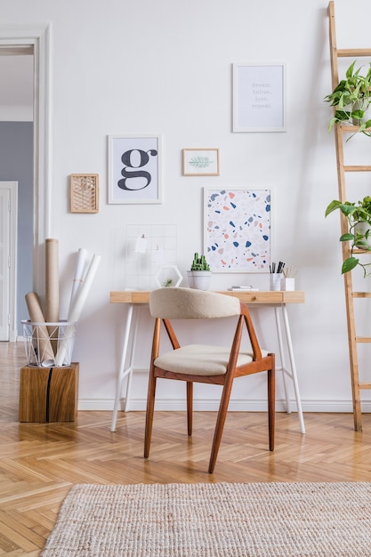 Composição criativa de design de interiores de escritório em casa escandinavo elegante com molduras de pôster, mesa de madeira, cadeira, plantas e acessórios. Paredes neutras, piso em parquet.