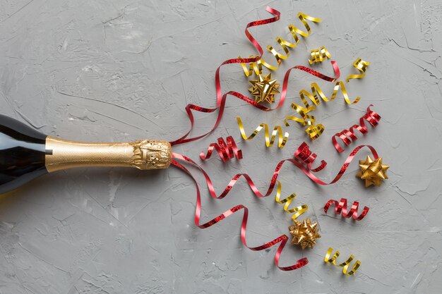 Composição criativa plana leiga com garrafa de champanhe e espaço para texto na cor de fundo Garrafa de champanhe com férias coloridas de serpentinas de festa ou conceito de natal