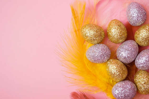 Composição da páscoa Ovos dourados e prateados da páscoa com penas coloridas em um fundo rosa Vista superior plana com espaço de cópia