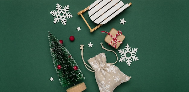 Composição de ano novo e Natal de flocos de neve brancos, árvore de chrismas decorativos e trenó em fundo de papel verde. Vista superior, copie o espaço.