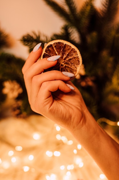 Composição de Ano Novo Mãos de mulheres com laranja seca perto da árvore de Natal