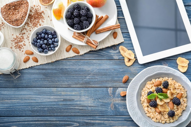 Composição de aveia saborosa com frutas e tablet em fundo de madeira