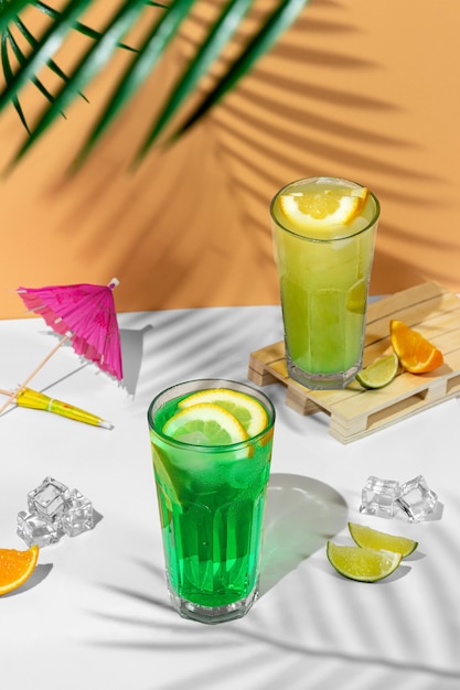 Composição de bela natureza morta com dois copos transparentes de bebida de verão. limonada verde com lima, hortelã, limão e frutas cítricas em um fundo tropical com sombras de uma palmeira