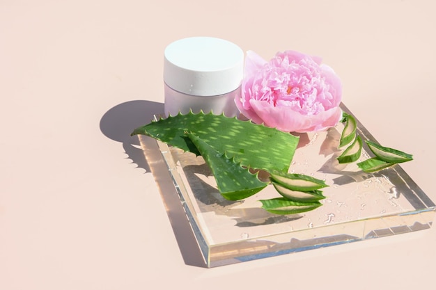 Composição de beleza estilizada frasco de creme de pele flor peônia folha de aloe vera no pódio de vidro conceito de spa de cosméticos orgânicos