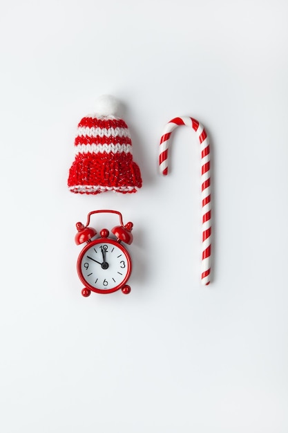 Composição de cana de Natal doce pequeno relógio analógico chapéu listrado em fundo branco estilo minimalista