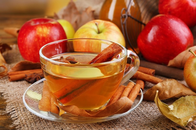 Composição de cidra de maçã com canela, maçãs frescas e folhas de outono em fundo de madeira