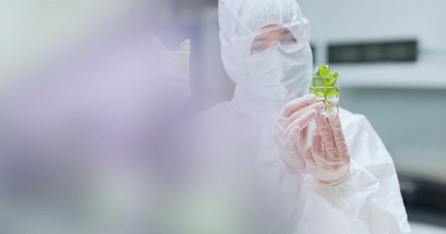 Composição de cientista feminina em traje de ppe segurando um copo com planta em laboratório