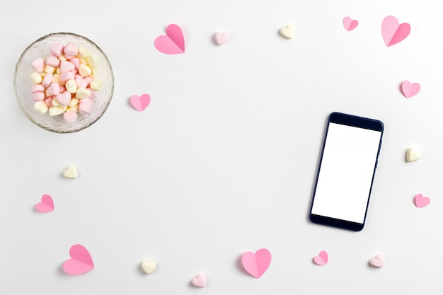 Composição de corações rosa feitos de papel, marshmallows em forma de coração e um telefone