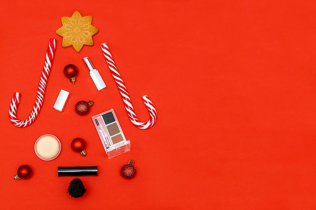 Composição de cosméticos de beleza de ano novo em forma de árvore de Natal com pincéis batom sombra em pó acessórios decorações de bolas em fundo vermelho Elegante Flat lay mock up vista superior com espaço de cópia