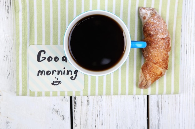 Foto composição de croissant fresco de café e cartão de papel em guardanapo em fundo de madeira