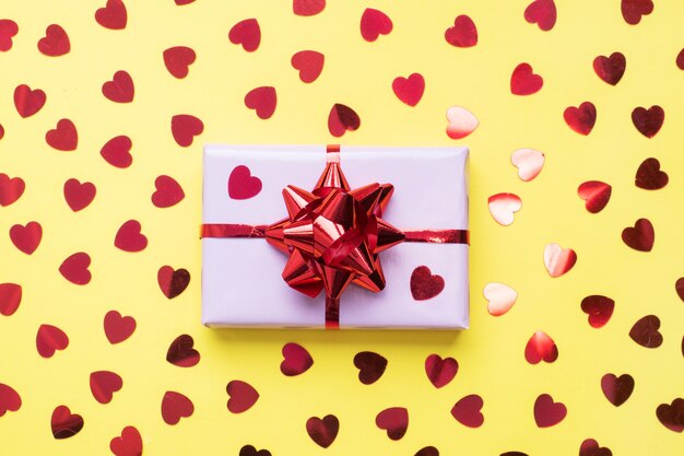 Composição de dia dos namorados, caixa de presente de saudação com corações de confete em fundo amarelo. Postura plana.