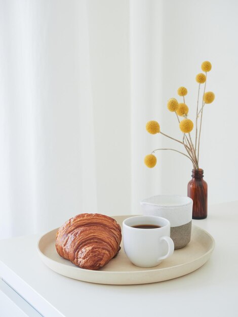 Composição de estilo de vida minimalista para o café da manhã Bandeja com croissant de jarro de leite e garrafa âmbar com flores amarelas