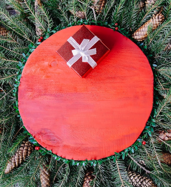 Composição de férias de inverno de Natal e ano novo com superfície de madeira vermelha em galhos de árvore verde do abeto, fatias de laranja secas, cones, caixa de presente e laço vermelho.