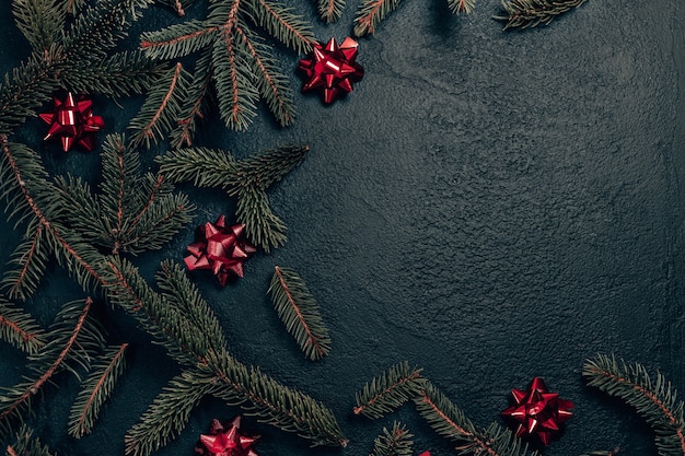 Composição de férias de Natal com ramo de pinheiro e laços vermelhos em fundo escuro. Camada plana, vista superior, espaço de cópia.