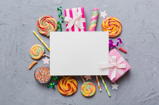 Foto composição de férias plana papel em branco pirulito decorações de aniversário em fundo colorido vista superior espaço de cópia para texto