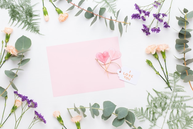 Composição de flores. Papel em branco, flores de cravo, galhos de eucalipto em fundo pastel. Camada plana, vista superior.