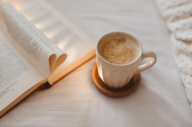 Composição de manhã aconchegante com uma xícara de café e um livro na cama