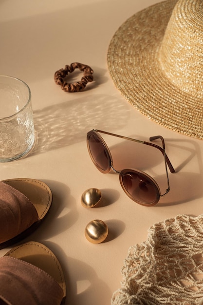 Composição de moda estética boêmia de luxo com vidro de cristal em sombras de luz solar cintilantes Óculos de sol chapéu de palha feminino saco de corda brincos dourados em fundo bege neutro