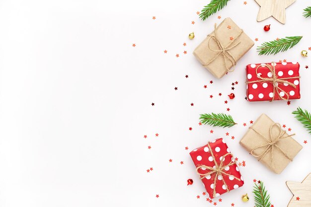 Foto composição de natal com caixas de presente, galhos de árvores de abeto, enfeites e confetes em fundo branco.