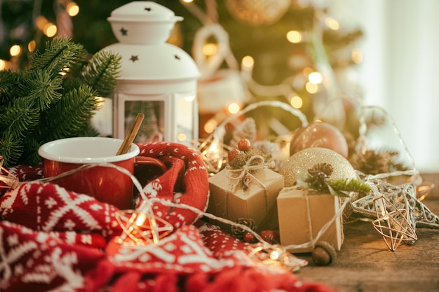 Composição de natal com copo vermelho de chocolate, cachecol, lanterna, pisca-pisca e bolas