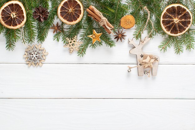 Composição de natal com galhos de uma árvore de natal e decorações econaturais laranja canela em um fundo branco de madeira