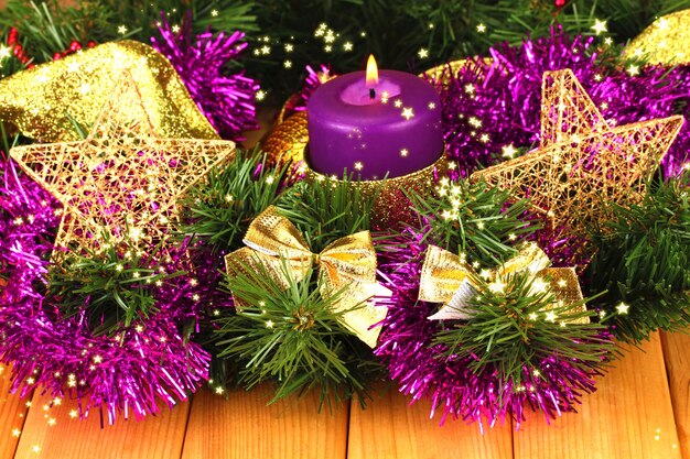 Composição de Natal com velas e enfeites nas cores roxa e dourada em fundo de madeira.