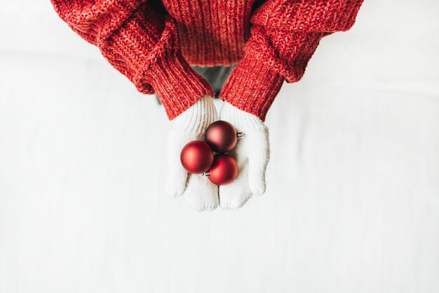 Composição de natal de ano novo de natal. mulher jovem com uma camisola de malha vermelha e luvas brancas segurando uma árvore de brinquedos de natal vermelhos