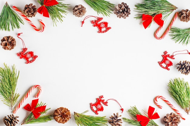 Composição de Natal. Galhos de árvore do abeto, brinquedos de Natal de madeira vermelha, arcos, bastões de doces em fundo branco.