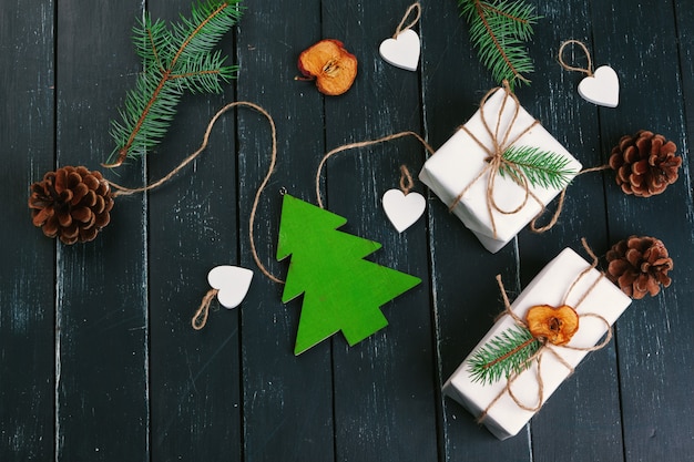 Composição de Natal. Presente de Natal, manta de malha, pinhas, galhos de pinheiro em fundo de madeira.