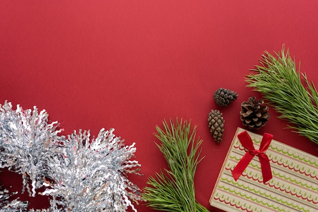 Composição de Natal. Uma caixa com um presente e ramos de abeto em um fundo vermelho. Cones de abeto e decorações de Natal. Camada plana, vista superior, espaço para texto