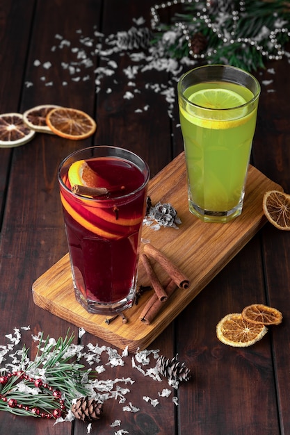 Composição de natureza morta com dois copos de bebida refrescante de inverno vermelha e verde ou vinho quente com fatias de laranja em um fundo escuro de madeira com neve