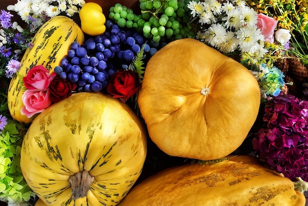 Composição de outono brilhante de legumes, frutas e flores. melões de diferentes tamanhos, marmelo, uvas, flores silvestres, rosas em uma mesa de madeira. vista superior, close-up.