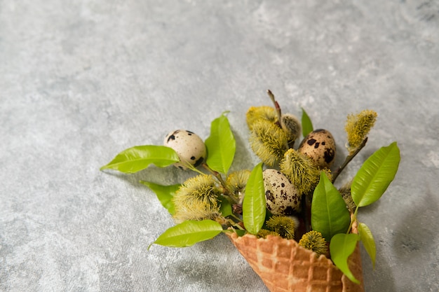 Composição de Páscoa ovos de codorna e galhos de salgueiro em um cone de waffle em uma parede cinza.