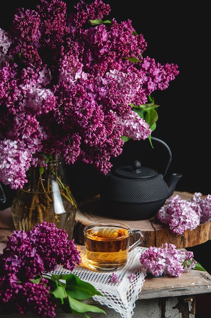 Composição de primavera com um buquê de lilases em um jarro lilás bule de ferro fundido em uma mesa vintage Flores lilás Sombras suaves volumétricas Low key