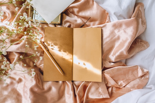 Composição de primavera, flores de gipsófila brancas com caderno e caneta no tecido de cetim dourado