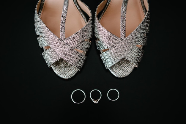 Composição de sapatos e anéis de prata isolada no fundo preto Noiva acessória Calçado Anéis de casamento e sandália Sapato com cristal Close up Flat lay Vista superior Noivado