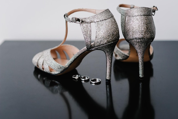Composição de sapatos e anéis de prata isolada no fundo preto Noiva acessória Calçado Anéis de casamento e sandália Sapato com cristal Fechar noivado